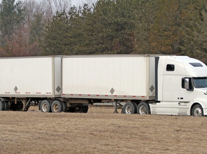 Semi tractor trailer truck on a highway hauling two trailers connected with a second fifth wheel, commonly called a B-Train.  16:9 aspect ratio.